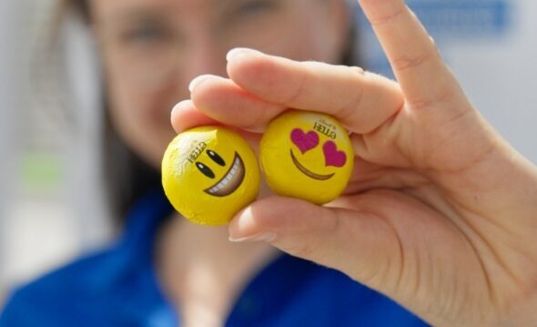 Auf diesem Bild sehen Sie eine Mitarbeiterin, die zwei im Emoji-Design verpackte Stück Schokolade in der Hand hält.