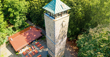 Vierlingsturm und Strobelhuette auf dem Fischerberg Die Fotoaufnahme zeigt von oben betrachtet den Vierlingsturm und die Strobelhuette auf dem Fischerberg. Rings herum ist grüner Wald im Sonnenschein zu sehen.