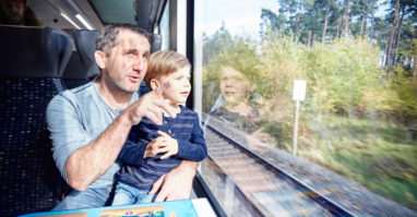 Auf dem Bild sieht man einen Mann mit seinem Kind. Beide schauen aus dem Fenster der oberpfalzbahn.