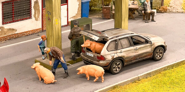 Ansicht der Miniaturwelt Kolejkowo. Man sieht ein Schweinetransport in einem Auto an einer Tankstelle.