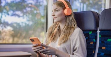 Reisende im trilex hört Musik Eine junge Frau sitzt mit Handy und Kopfhörern im trilex und hört Musik, während sie aus dem Fenster schaut.