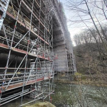 Das Bild zeigt die Elstertalbrücke während der Renovierung, umgeben von einem großen Gerüst entlang eines Flusses.